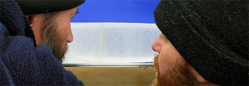 Two RECAP scientists, Johannes Freitag and Bo M. Vinther, study a visible layer in the ice core. The layer appears light brown / yellow in the picture, but consists of small particles that are dark brown or black.  The layer is likely of volcanic origin, as increased acidity was detected close to the visible layer. 