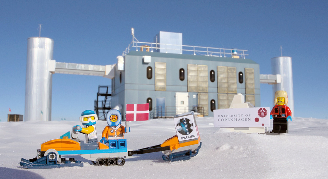 LEGO-IceCubers vajer med Dannebrog og Københavns Universitets skilt foran IceCube Lab på Sydpolen. Foto: Marc Jacquart, taget under hans overvintring på Sydpolen.
