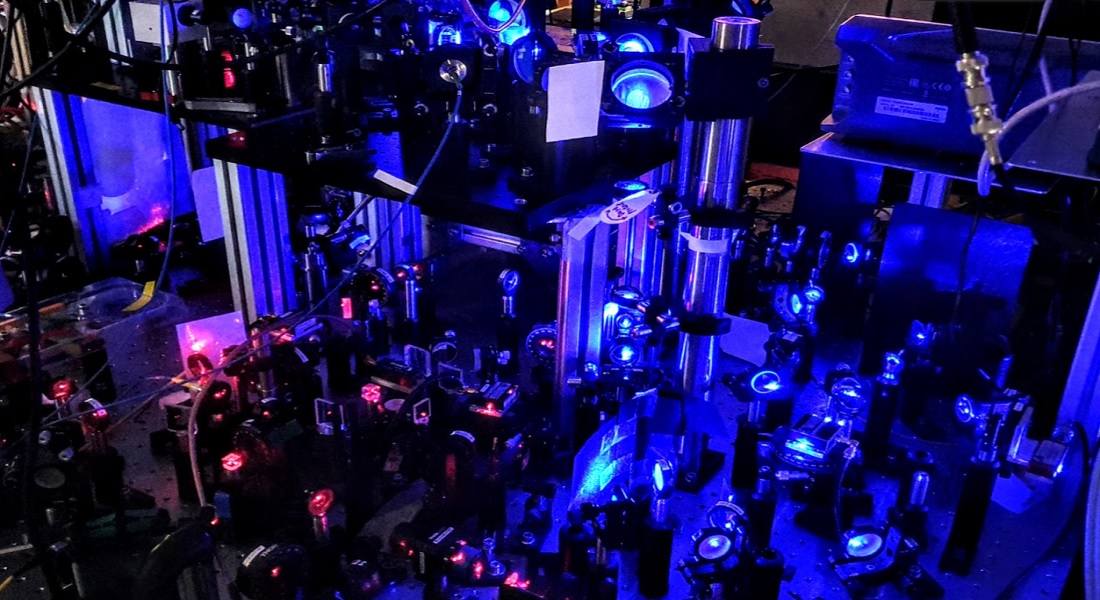 Laserlys, spejle og linser. Den blå laser køler atomerne i vakuumkammeret, og den røde bliver brugt til at probe atomerne og undersøge superradiens.