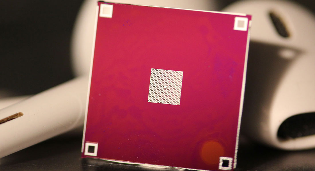 A thin silicon nitride membrane (white) is stretched tight across a silicon frame (red).  The membrane contains a pattern of holes, with one small island in the center, whose vibrations are measured in the experiment.