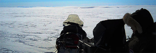 Iben inspecting the radar data capture computer under the black “hood” during measurements a few km south of camp. In the background, one can just see beginning of one of the ice streams that drain the Renland Ice Cap. Iben inspecting the radar data capture computer under the black “hood” during measurements a few km south of camp
