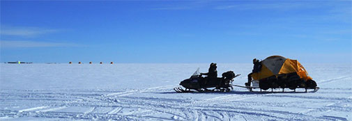 Bags with polar gear and personal equipment on the sled with a tent and a team member on top. In the background the main RECAP camp, located a little more than 500 m away from the radar camp: This is the same distance as the length of the core we hope to drill over the next two months. Sled with gear and a tent