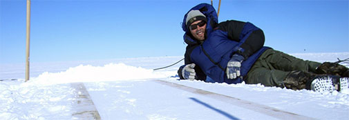 Chief driller Trevor resting after a job well done: The compacted snow holds the two beams in place that constitute the foundation of the deep ice-core drilling setup. Chief driller Trevor resting after a job well done