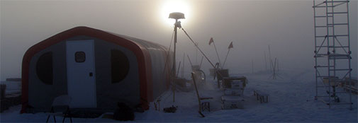 Early morning at RECAP. The sun has not set in weeks, but at night, the low sun is not strong enough to prevent fog from forming. Visibility often drops to less than 100 meters, and the camp becomes eerie The fog usually burns off before 9 am. The mast blocking the sun is the Iridium antenna that provides phone and data communications.
